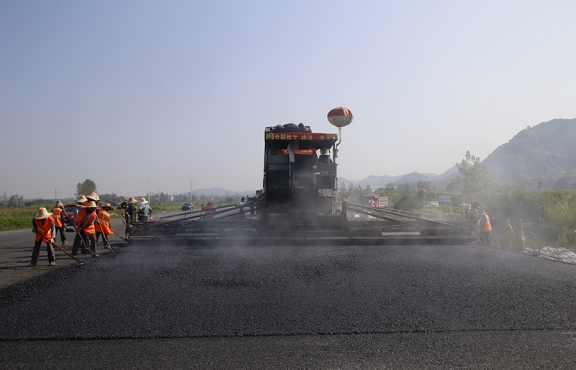 2019年8月，宜春經(jīng)開區(qū)S311路面攤鋪現(xiàn)場，工友們輔助路面兩側(cè)的分料、補(bǔ)窩等作業(yè)